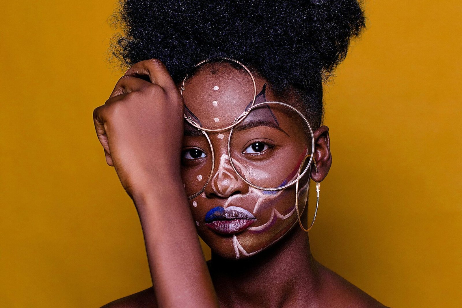 Artistic portrait of a woman with unique face paint against a vibrant backdrop.